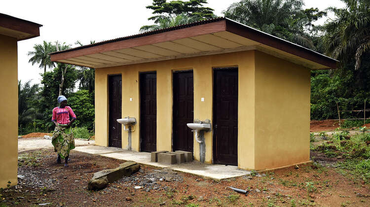2019-ebola-praevention-sierra-leone-toiletten_C_Kai-Loeffelbein-16-9.jpg A woman is walking by a toilet house.
