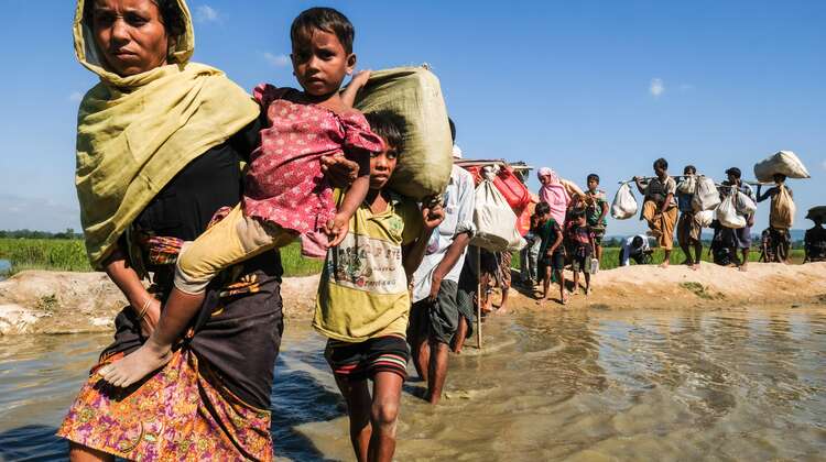 Eine lange Reihe von Frauen, Männern und Kindern waten durch einen Fluss