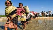 Eine lange Reihe von Frauen, Männern und Kindern waten durch einen Fluss