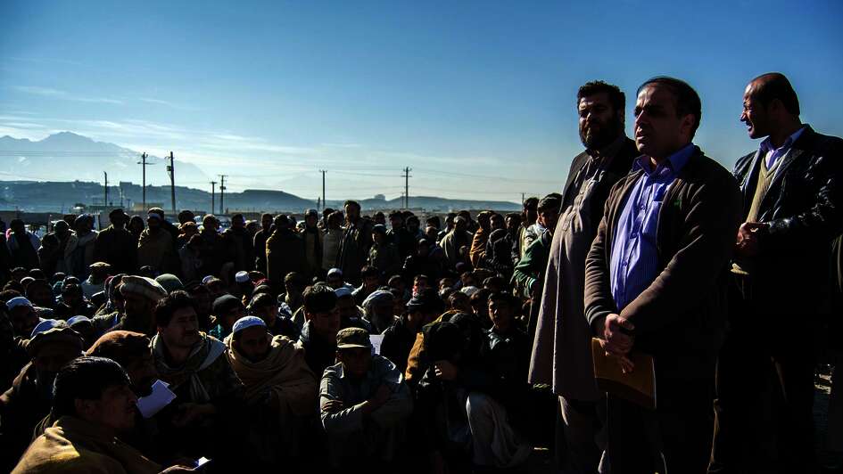 Flüchtlinge in Winterkleidung warten auf die Verteilung von Haushaltsgütern