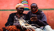 2021-agrishare-fatuma-oluke-mit-smartphone.jpg Zwei Landwirte in Uganda verwendet das Smartphone um Landarbeiter zu finden, 2021.