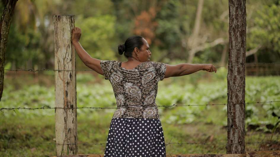Frau steht an Stacheldrahtzaun.