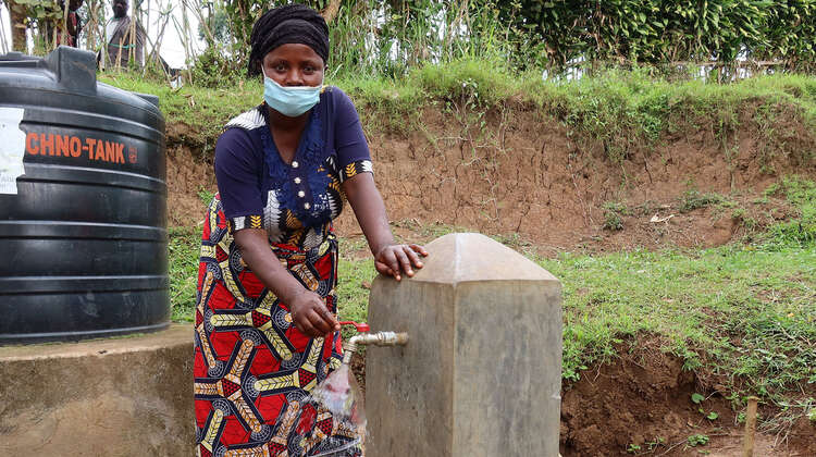 2021-congo-wasserversorgung-projektteilnehmerinn-chiza-abasabimana-benutzt-pumpe.jpg Eine Frau steht an einer Wasserpumpe, Kongo 2021.