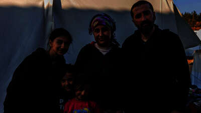 Erdbeben in der Türkei: Eine Familie steht vor einem Zelt, sie alle schauen in die Kamera.