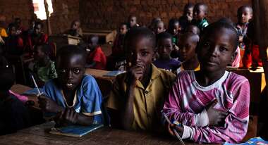 Drei Jungen sitzen im Vordergrund einer Schulklasse in Burundi