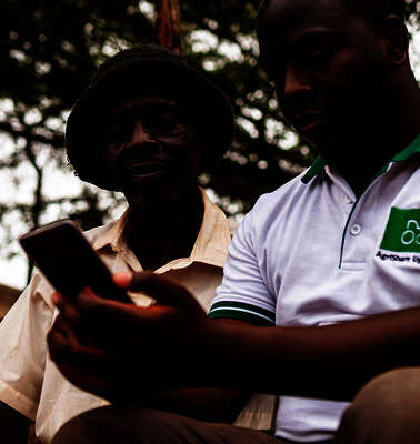 Zwei Kleinbauern schauen in ihr Smartphone und beschäftigen sich mit der Landwirtschafts-App AgriShare, Uganda 2021.